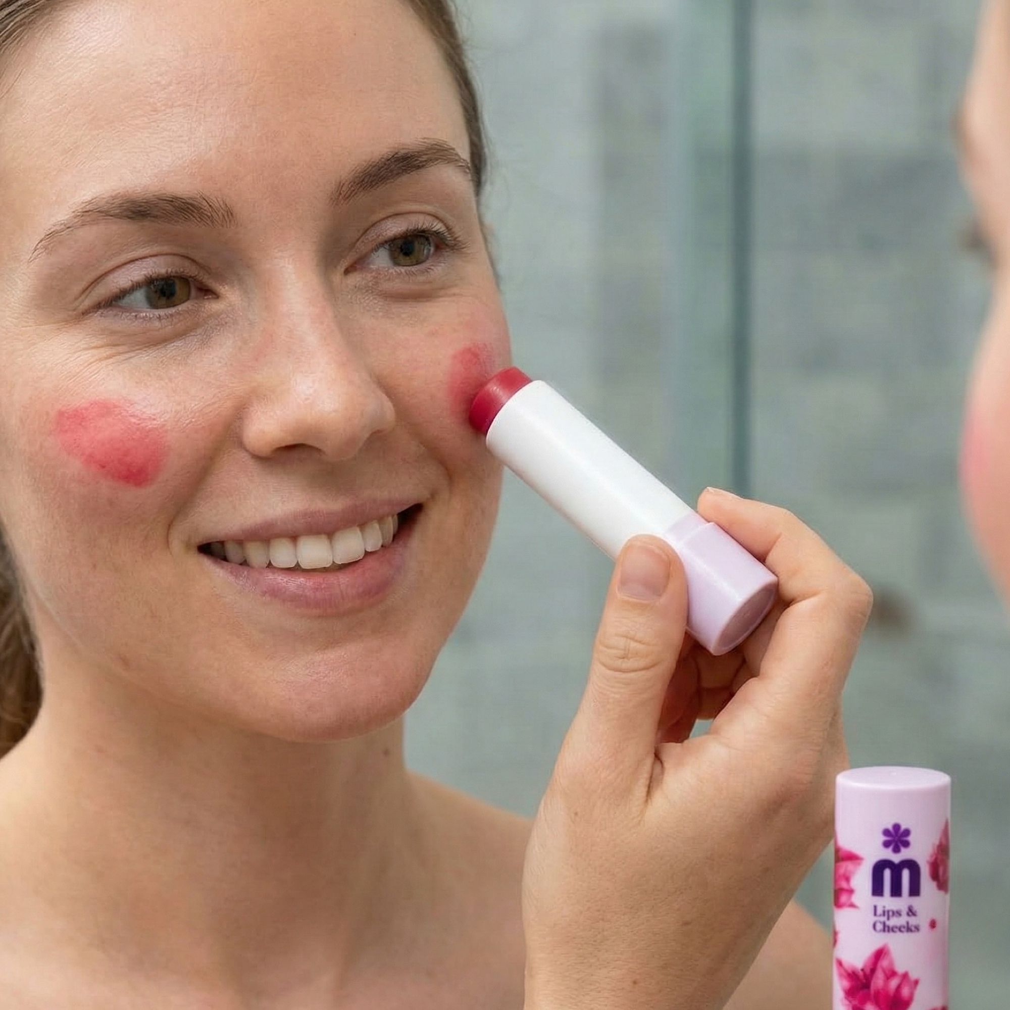 Frau trägt Lippen- & Wangenbalsam auf. Produktname: Melem Lips & Cheeks. Weißer Stift mit pinkfarbener Spitze. Spiegel im Hintergrund.