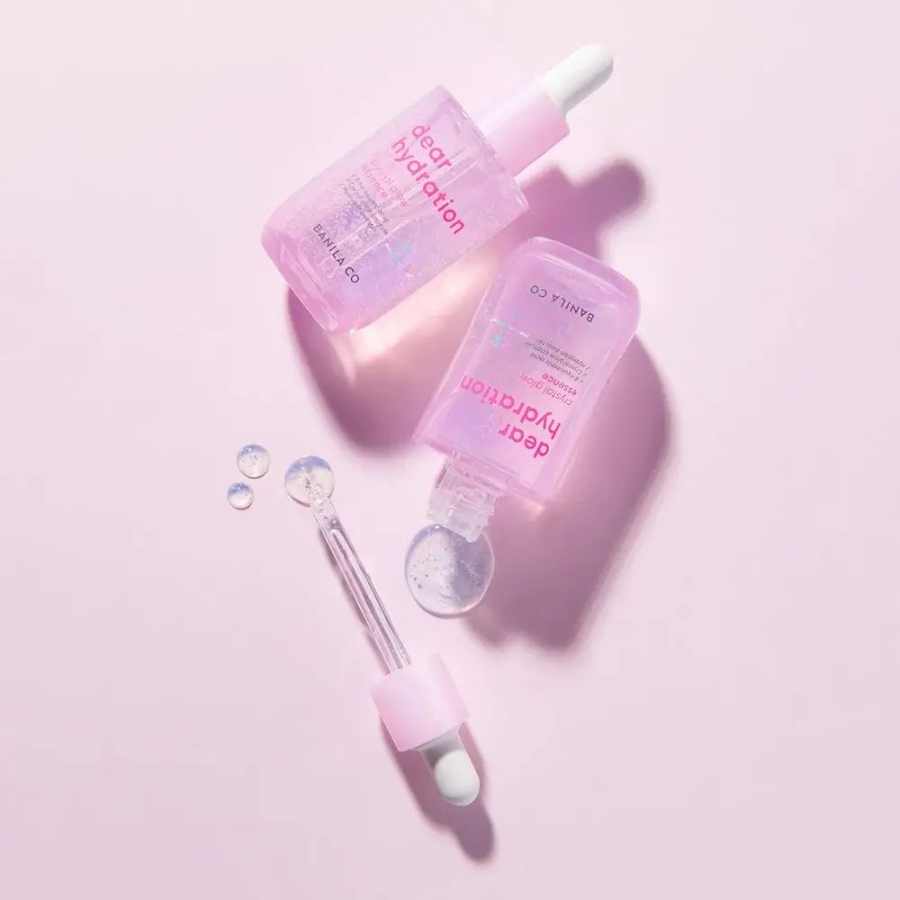 Zwei kleine durchsichtige Fläschchen mit rosa Pipettenaufsätzen, gefüllt mit einer hellvioletten Flüssigkeit. Beschriftung: "dear hydration".