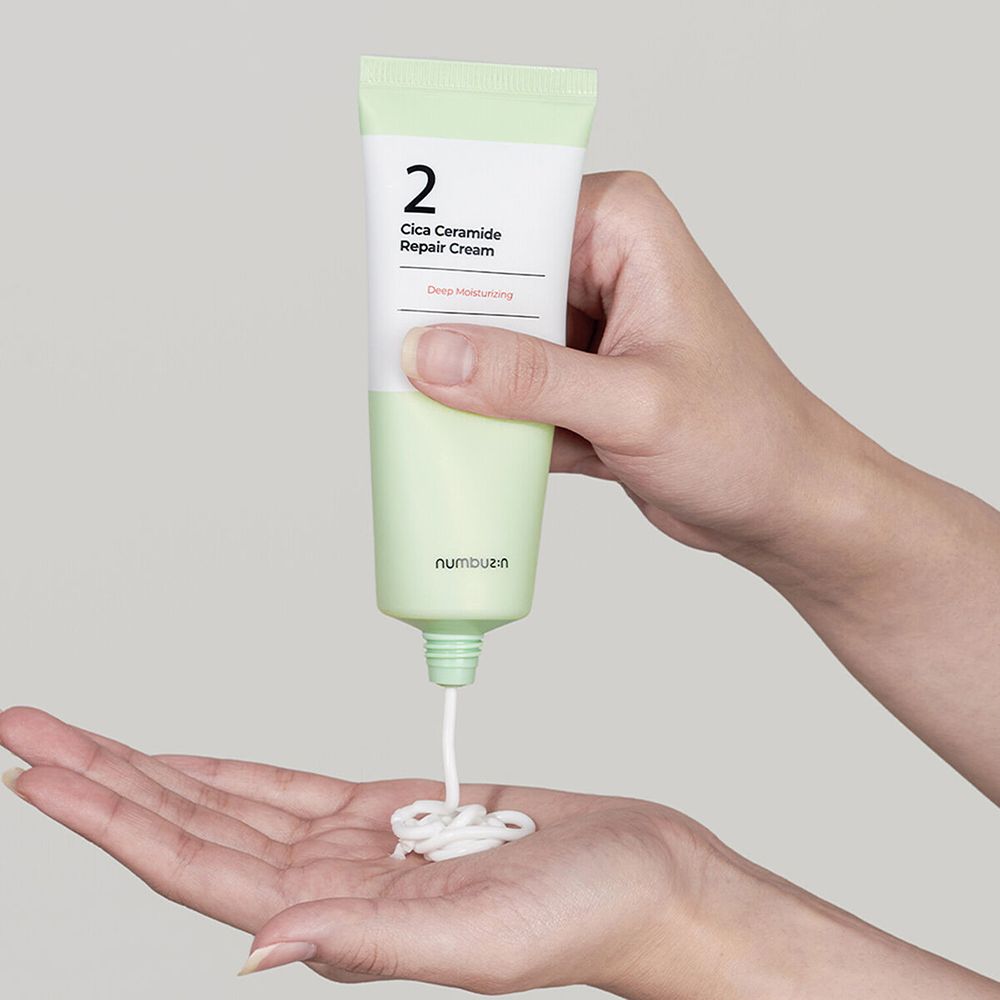 Hände halten einen Crèmetube, aus dem Creme austritt. Aufschrift: "2 Cica Ceramide Repair Cream". Marke: numbuz:n.