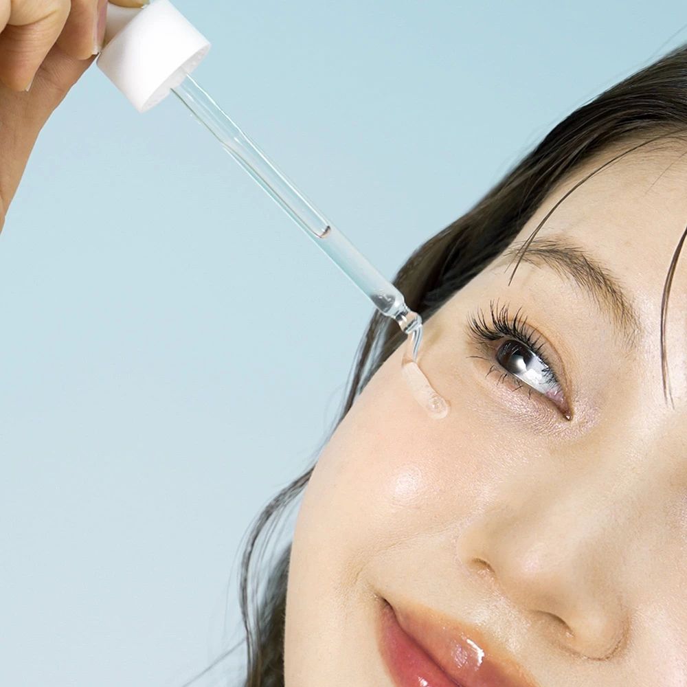 Frau mit Serum-Applikator. Serum wird auf die Haut aufgetragen. Blauer Hintergrund.