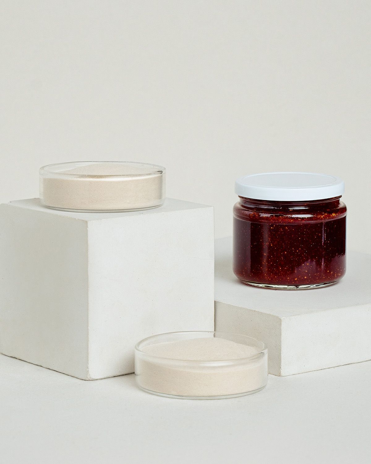Zwei Schalen mit Agar Agar Pulver und ein Glas Marmelade auf weißen Würfeln.