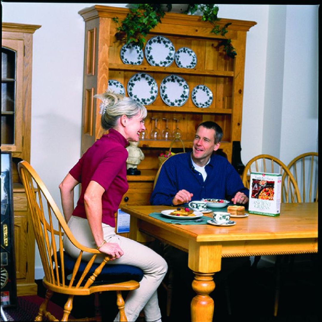 Frau und Mann sitzen an einem Tisch. Auf dem Tisch stehen Teller und eine Broschüre. Holzmöbel.
