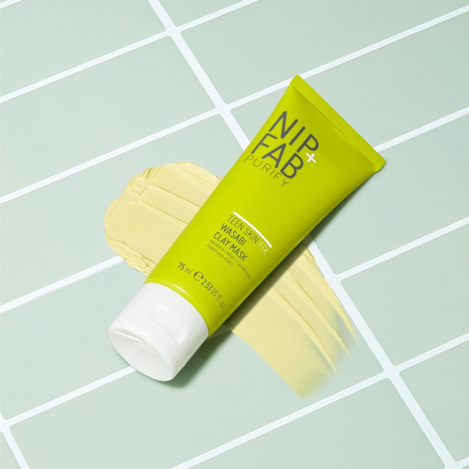 Grüne Tube und Maske auf Fliesen. Aufschrift: Nip+Fab, Teen Skin Fix Wasabi Clay Mask. 75 ml.