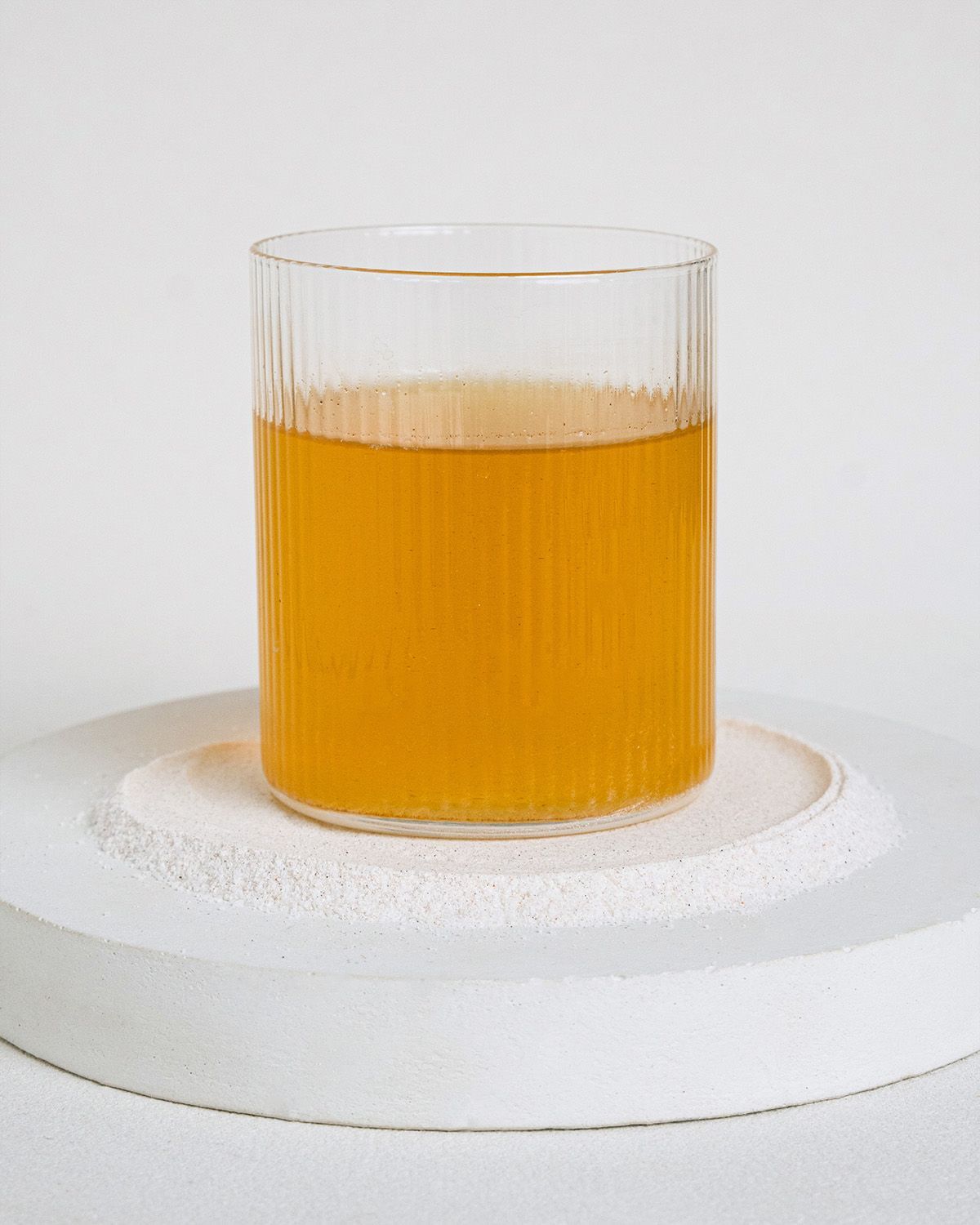 Ein Glas mit gelbem Elektrolytgetränk auf einem weißen Sockel.