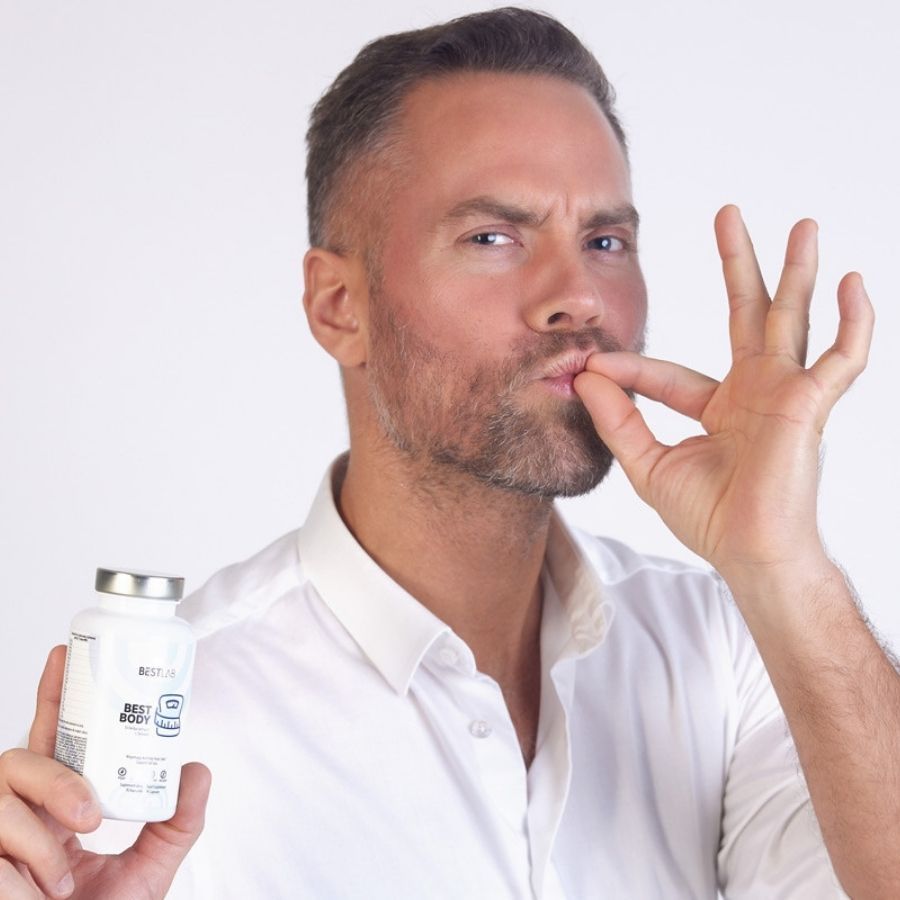 Mann hält weiße Flasche mit silbernem Deckel. Aufschrift: BEST LAB BEST BODY. Er deutet an, eine Kapsel zu nehmen.