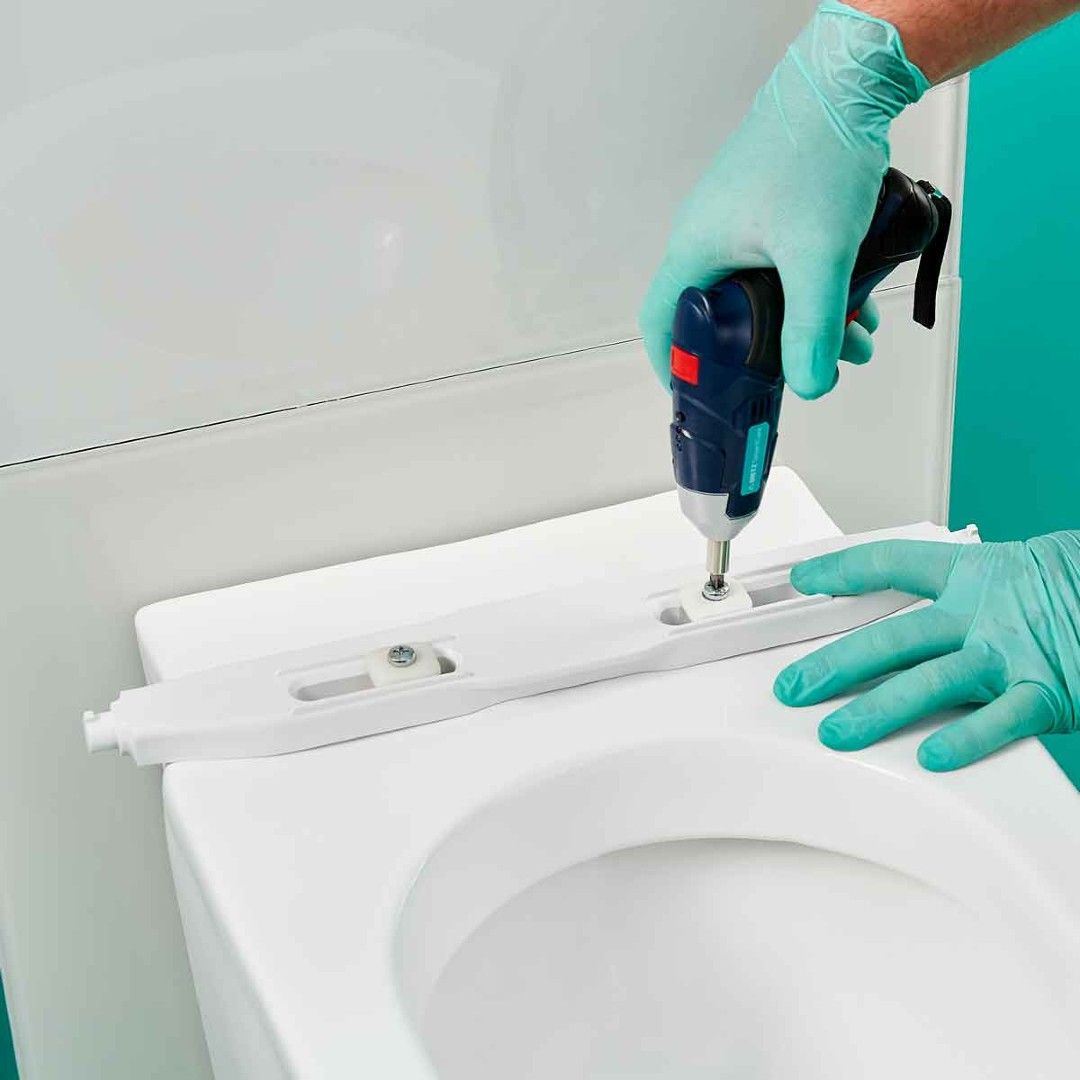 Hände mit Handschuhen montieren einen Toilettensitz mit Schraubendreher.