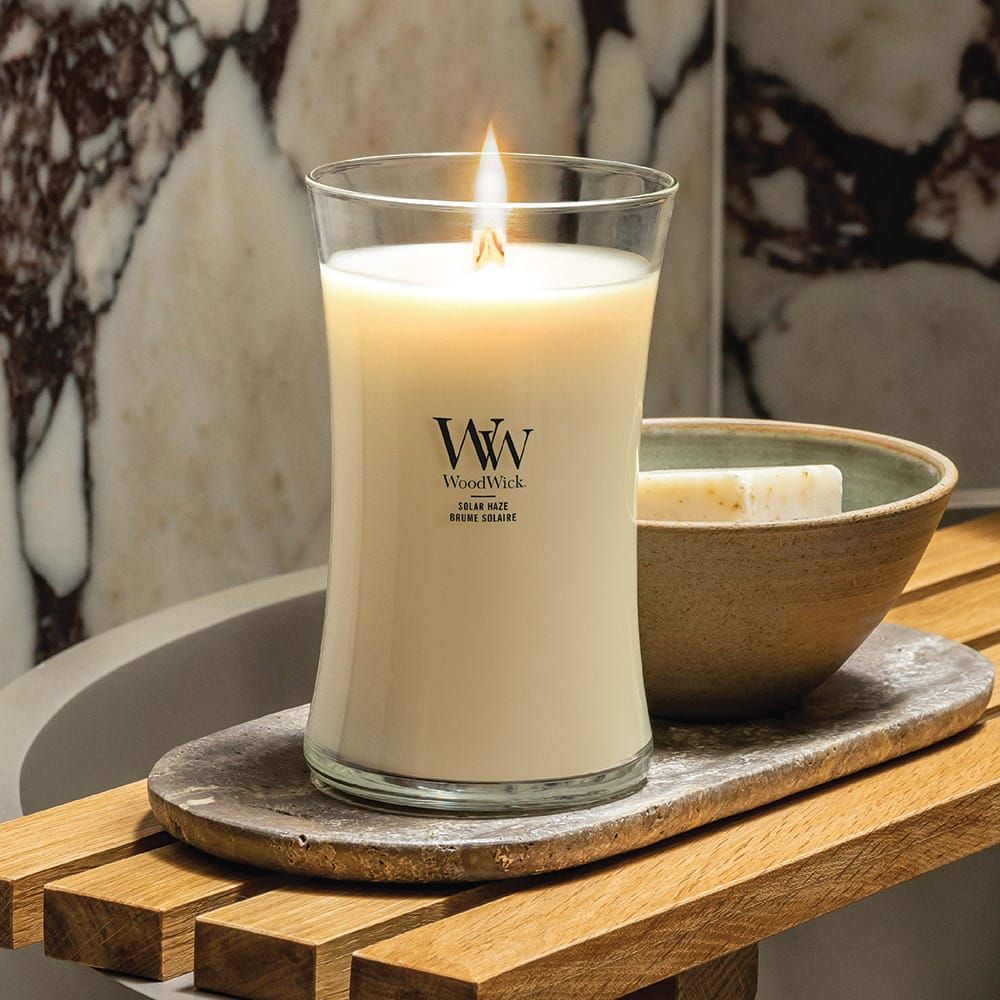 Kerzenglas mit Flamme. Aufschrift: WoodWick. Neben einem Seifenstück und einer Schale auf einem Holztablett.