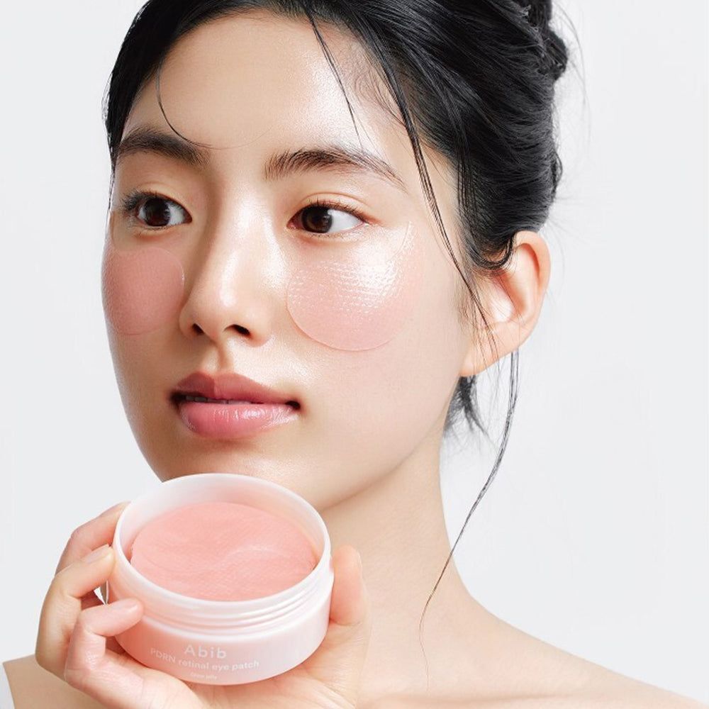 Frau hält eine offene Dose mit Augenpflastern. Auf der Haut sind Augenpflaster angebracht. Dose mit Aufschrift Abib.