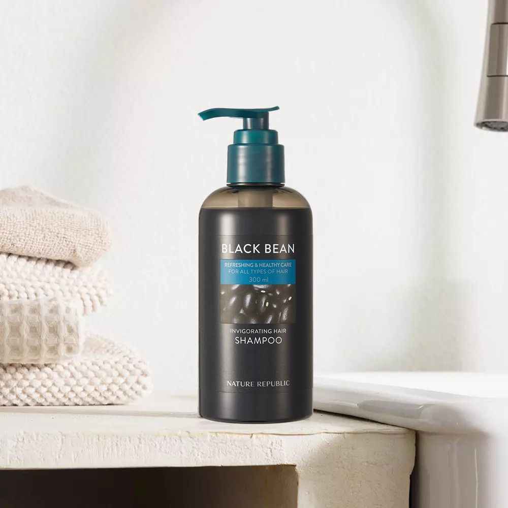 Schwarze Shampoo-Flasche mit Pumpe. Text: Black Bean, Invigorating Hair Shampoo, Nature Republic. Neben Handtüchern.