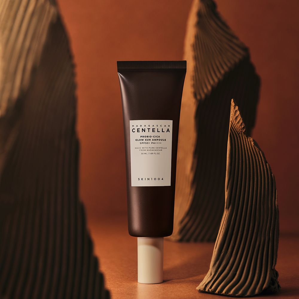 Braune Tube mit weißem Etikett. Text: MADAGASCAR CENTELLA, PROBIO-CICA GLOW SUN AMPULLE SPF50+ PA++++. Auf Sockel.