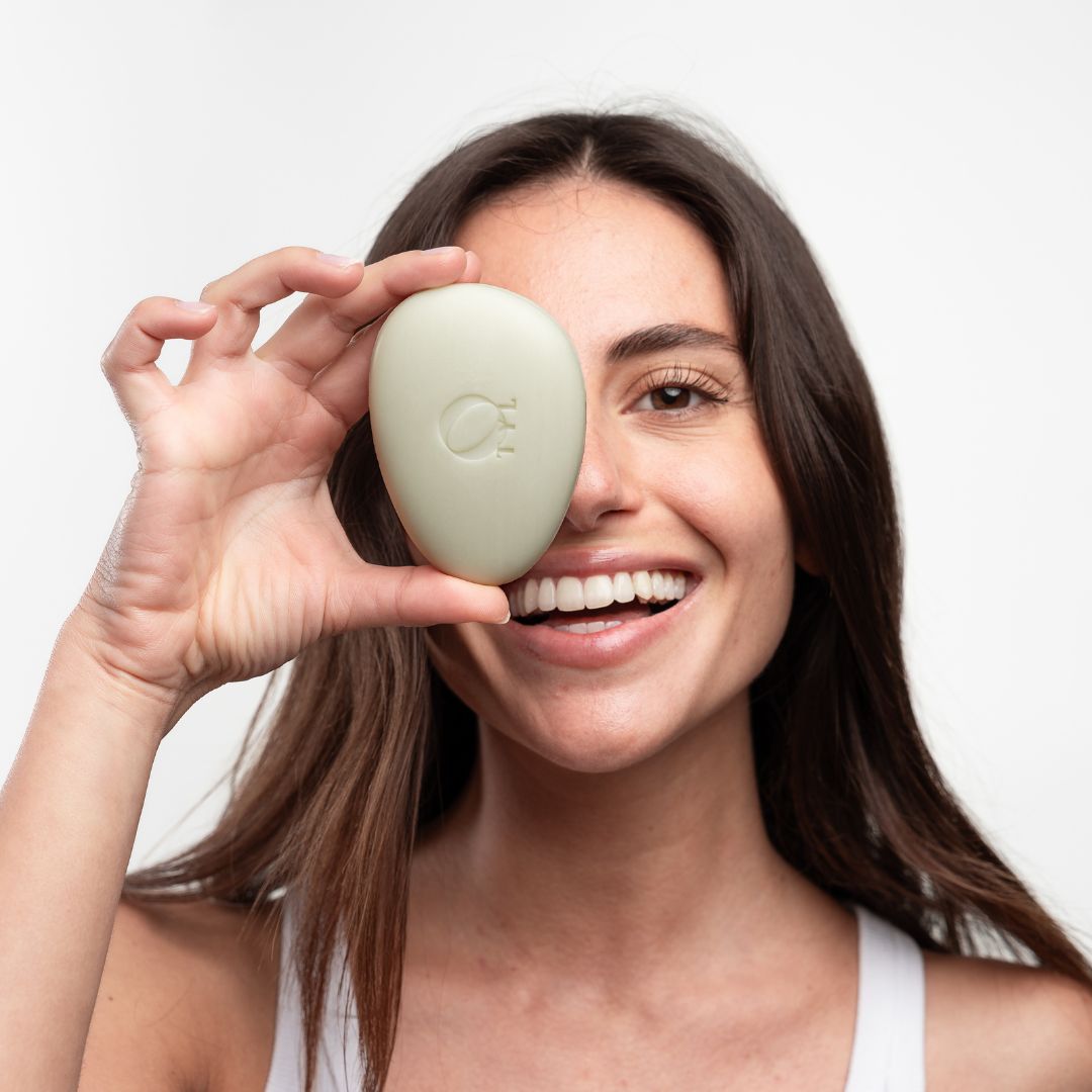 Helle, ovale Seife vor einem Auge. Frau lächelt. Seife mit Logo. 