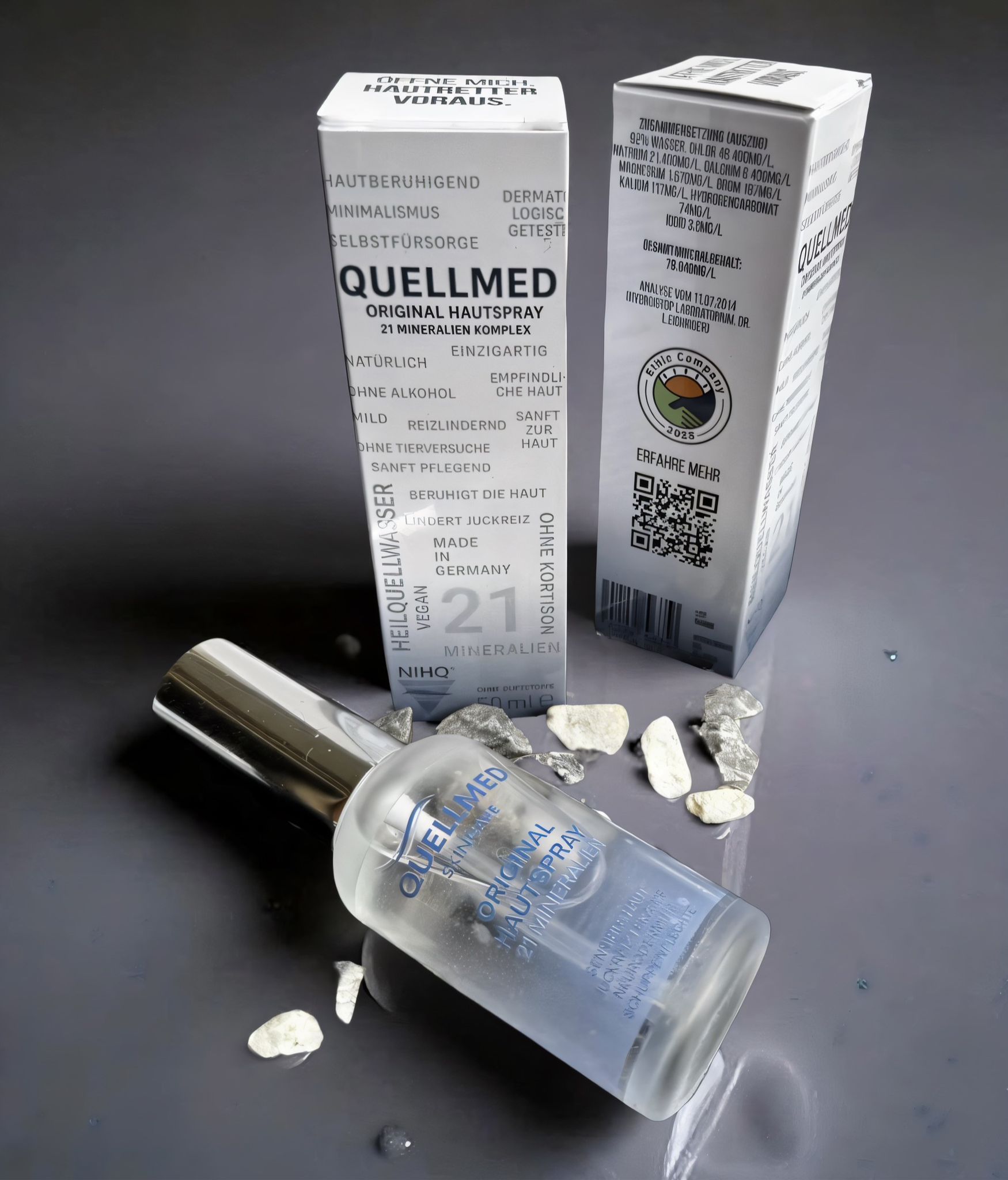 Produktflasche und Verpackung. Flasche liegt, Verpackung steht. Aufschrift: Quellmed Original Hautspray, 21 Mineralien Komplex.