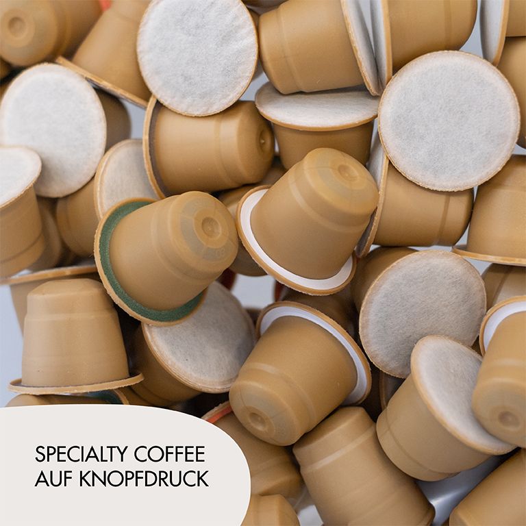 Kaffeekapseln. Viele Kapseln. Aufschrift: Specialty Coffee auf Knopfdruck. Kapseln braun, weißer Rand.