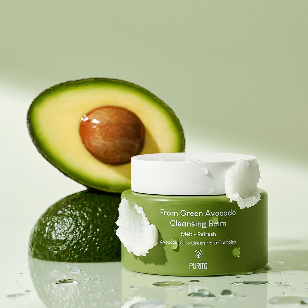 Grüner Tiegel neben halber Avocado und ganzer Avocado, auf nassem Untergrund.
