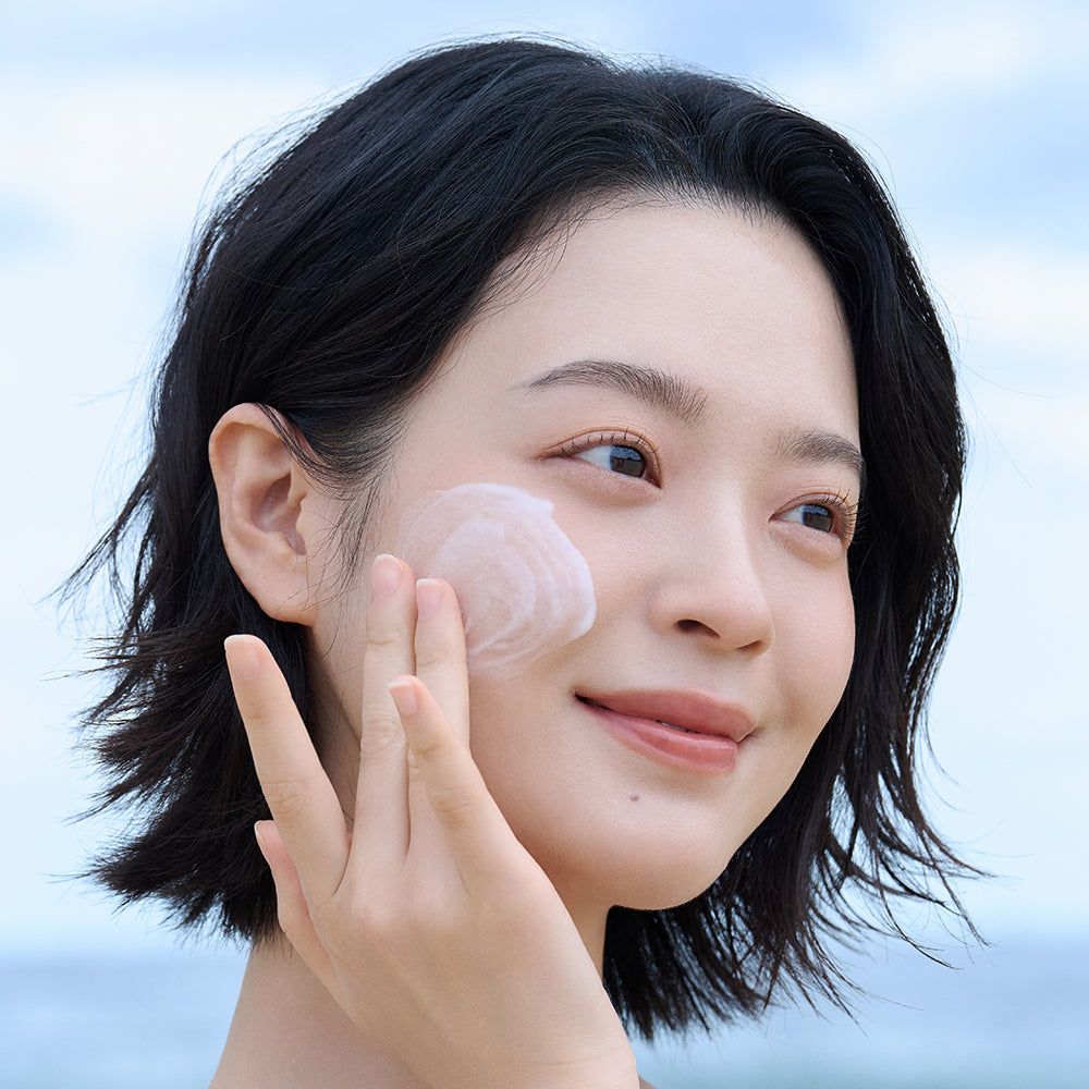 Gesicht einer Frau, die eine Creme auf die Haut aufträgt. Creme ist sichtbar. Keine Produktbezeichnung.