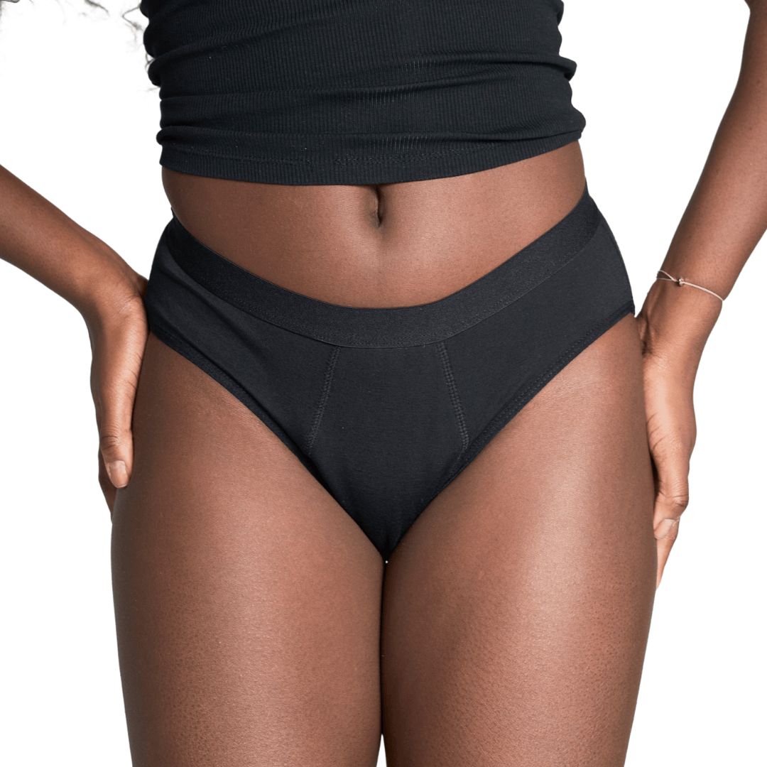 Schwarzer Slip. Blick auf den Unterleib einer Person. Der Slip bedeckt den Intimbereich.