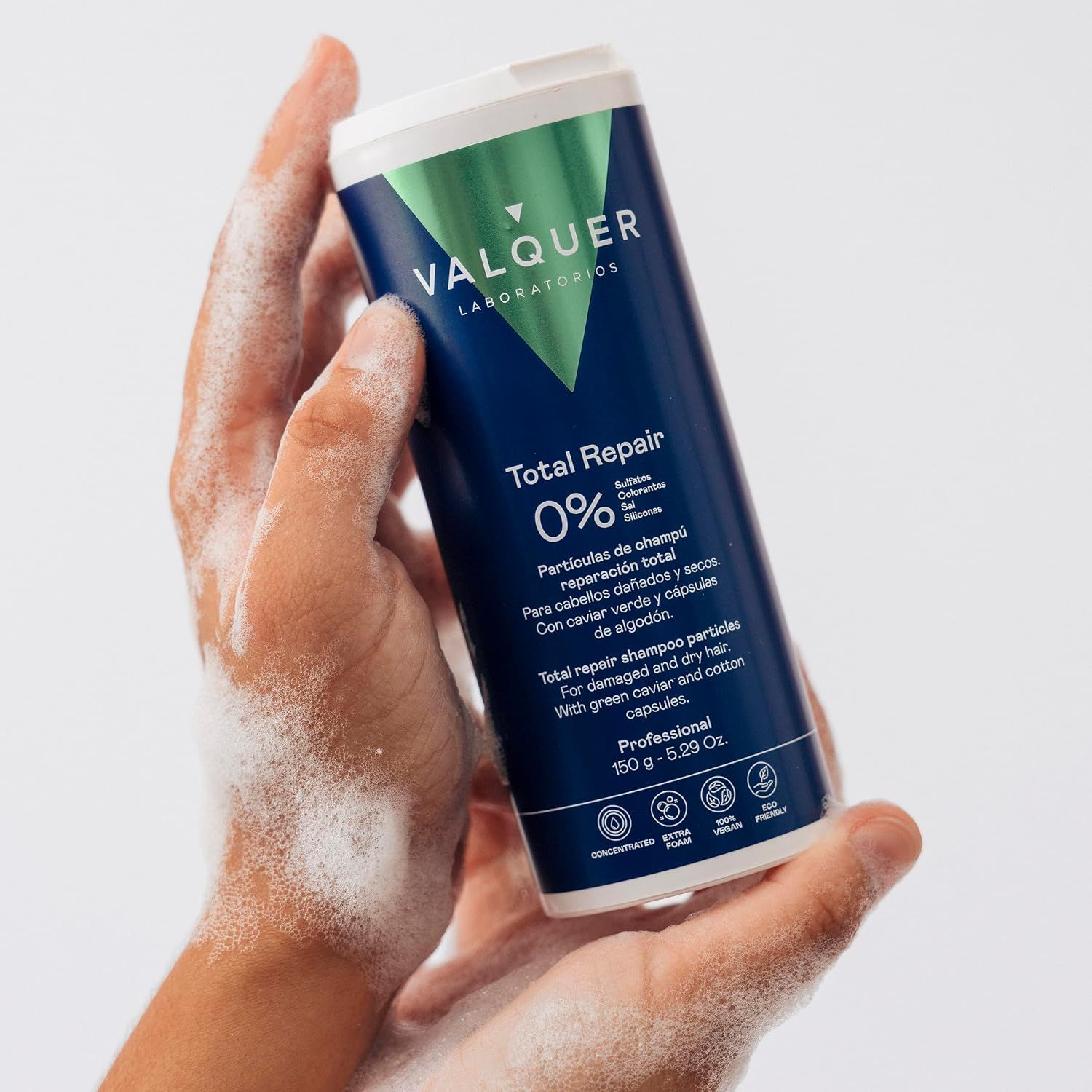 Hände halten eine dunkelblaue Flasche "Total Repair" Shampoo, während Schaum entsteht.