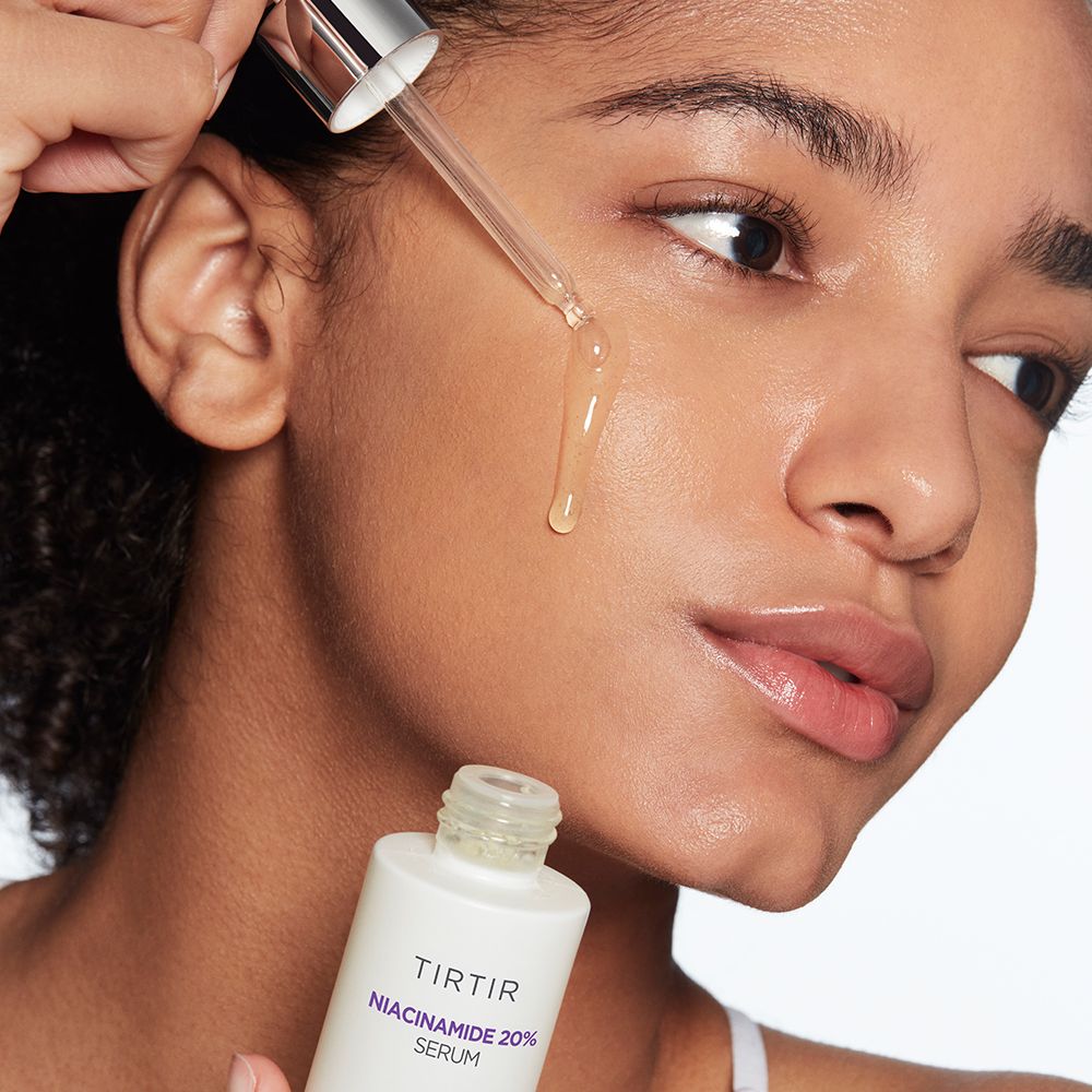 Frau trägt Serum mit Pipette auf. Flasche mit Aufschrift: TIR TIR Niacinamide 20% Serum. Hautnahaufnahme.