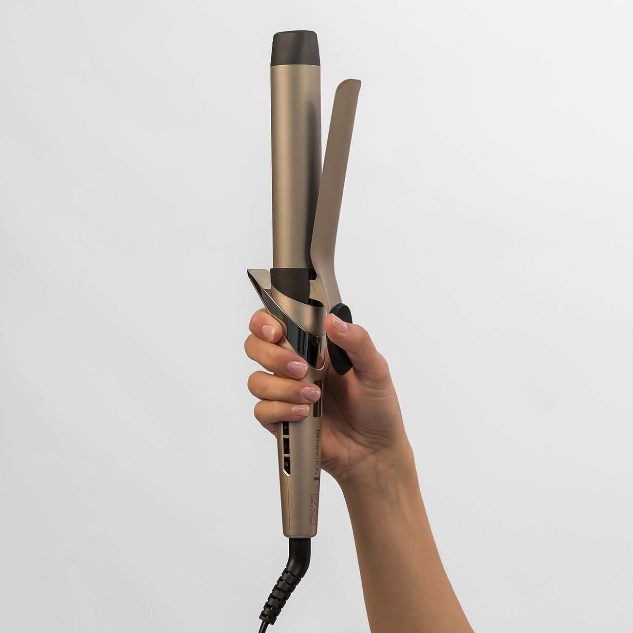 Hand hält einen goldenen Lockenstab mit schwarzem Griff und Kabel.