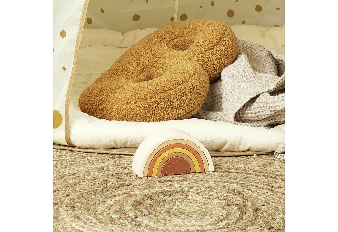 Regenbogen-Spielzeug aus Holz auf einem Teppich. Im Hintergrund ein Zelt und Kissen. Verschiedene Erdtöne.