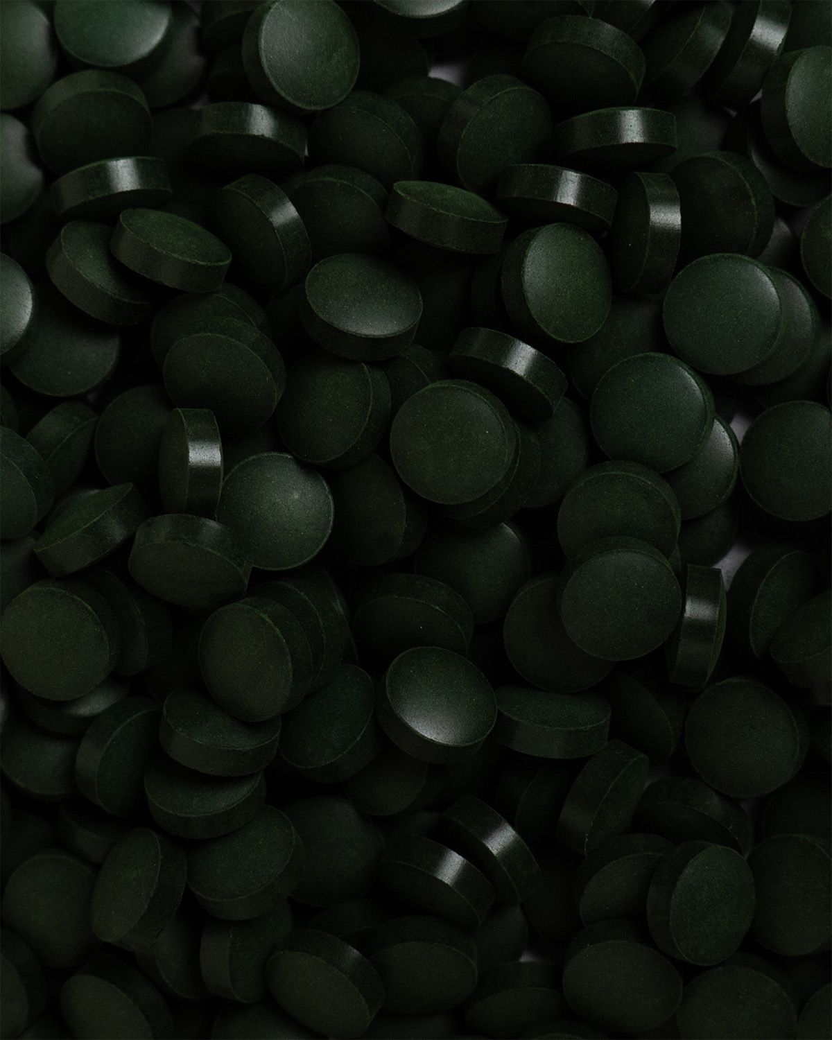 Nahaufnahme von vielen dunkelgrünen, runden Tabletten. Die Tabletten sind dicht gepackt.