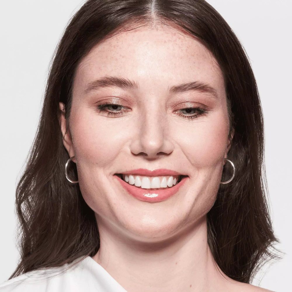 Frau mit hellbraunen Haaren, Lidschatten. Lächelt. Helle Haut. Ohrringe.