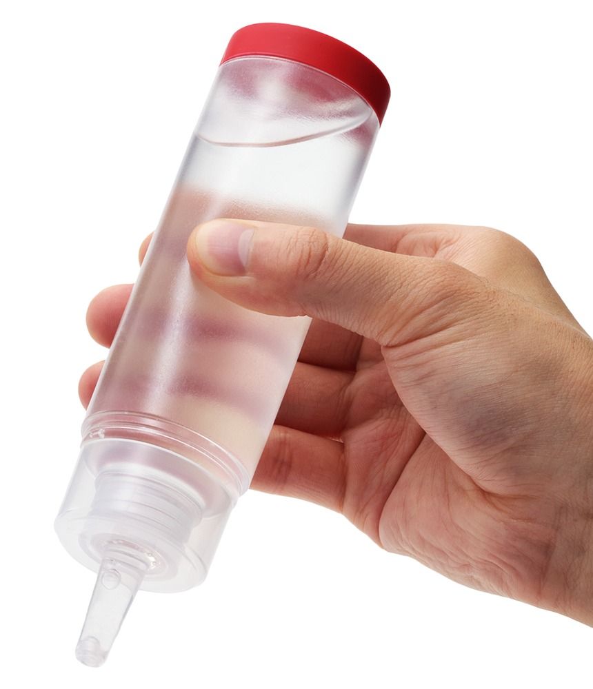 Transparente Flasche mit rotem Deckel, gehalten von einer Hand. Ausgießer sichtbar.
