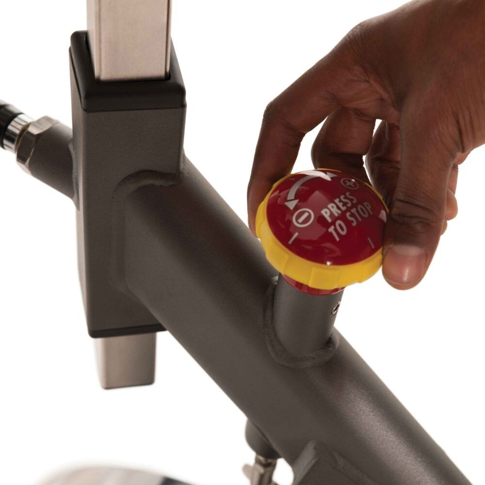 Nahaufnahme des Indoor Cycle. Roter Stoppknopf mit gelbem Ring. Aufschrift: PRESS TO STOP. Grauer Rahmen.