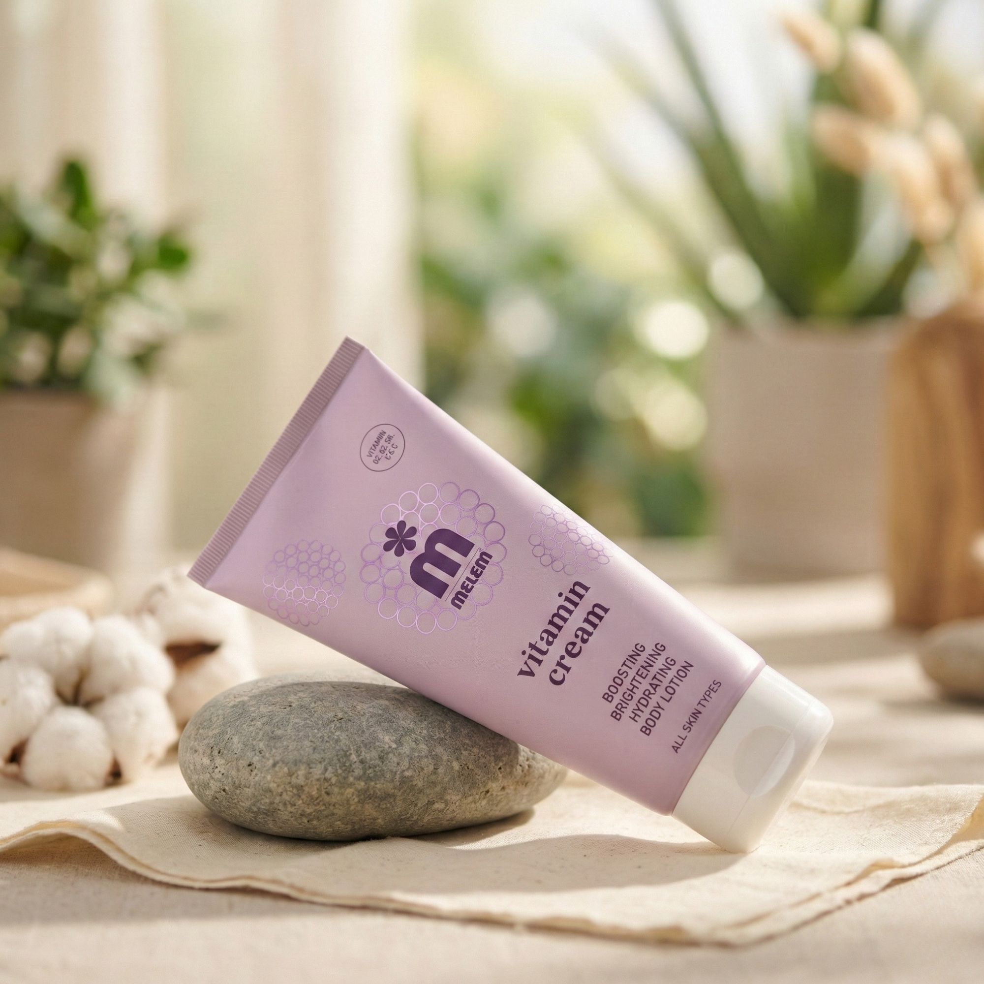 Rosa Tube mit weißem Deckel. Aufschrift: Melem Vitamin Cream. Liegt auf einem Stein. Im Hintergrund: Pflanzen und Baumwolle.