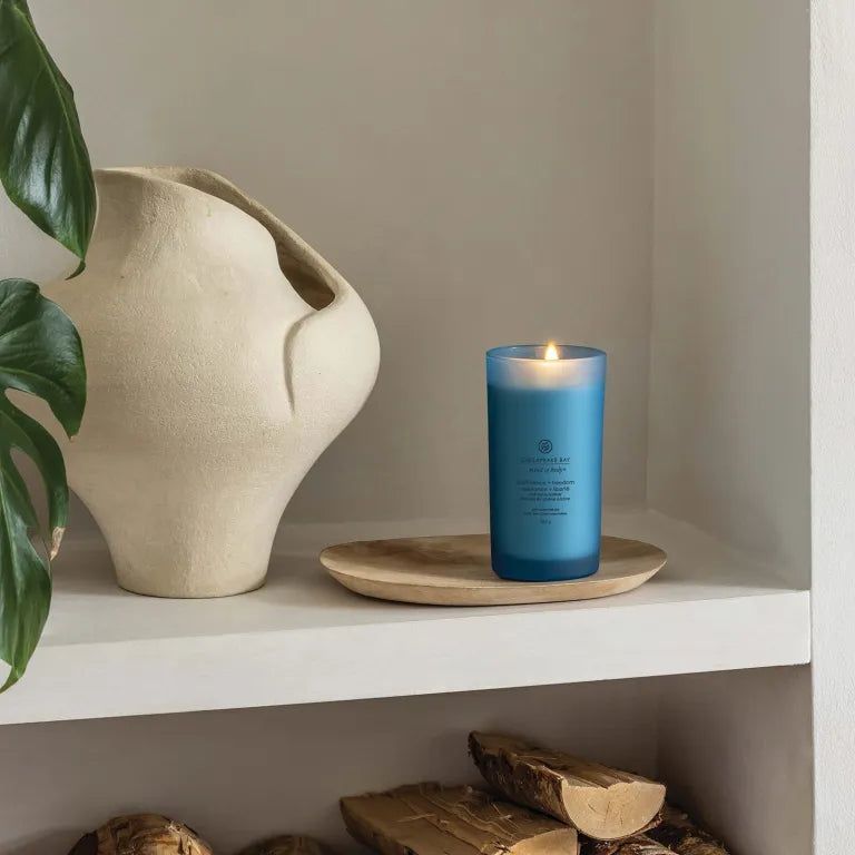 Blaue Kerze auf Holztablett, brennend. Chesapeake Bay, mind & body, confidence + freedom. Auf Regal.