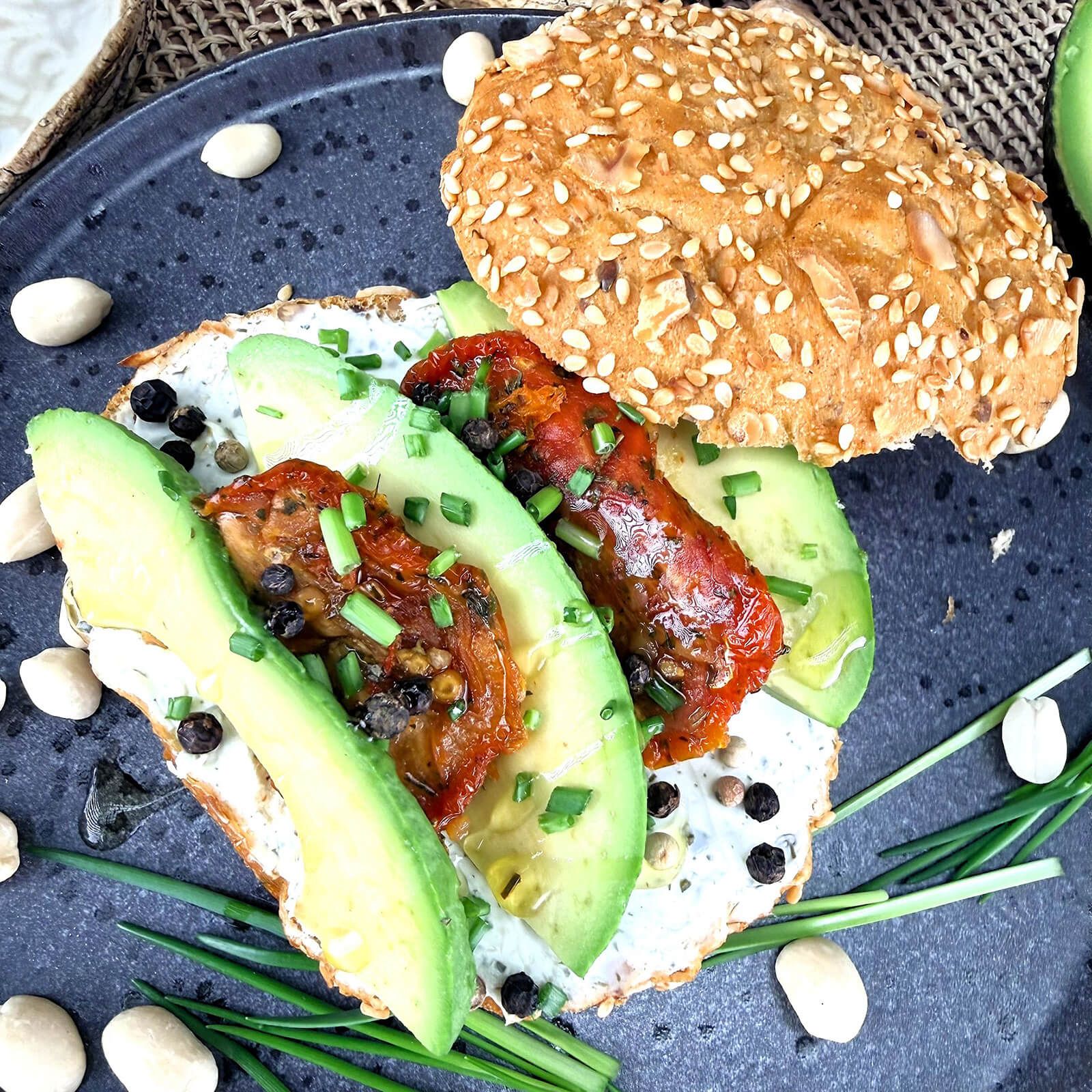 Locawo Erdmännchen Brötchenhälfte belegt mit Avocado, getrockneten Tomaten und Kräutern.