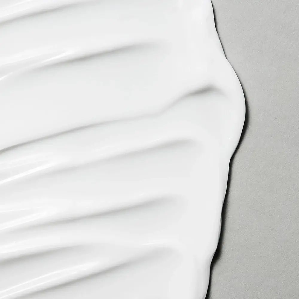 Nahaufnahme von weißer Creme. Die Textur ist glatt und wellig. Grauer Hintergrund.