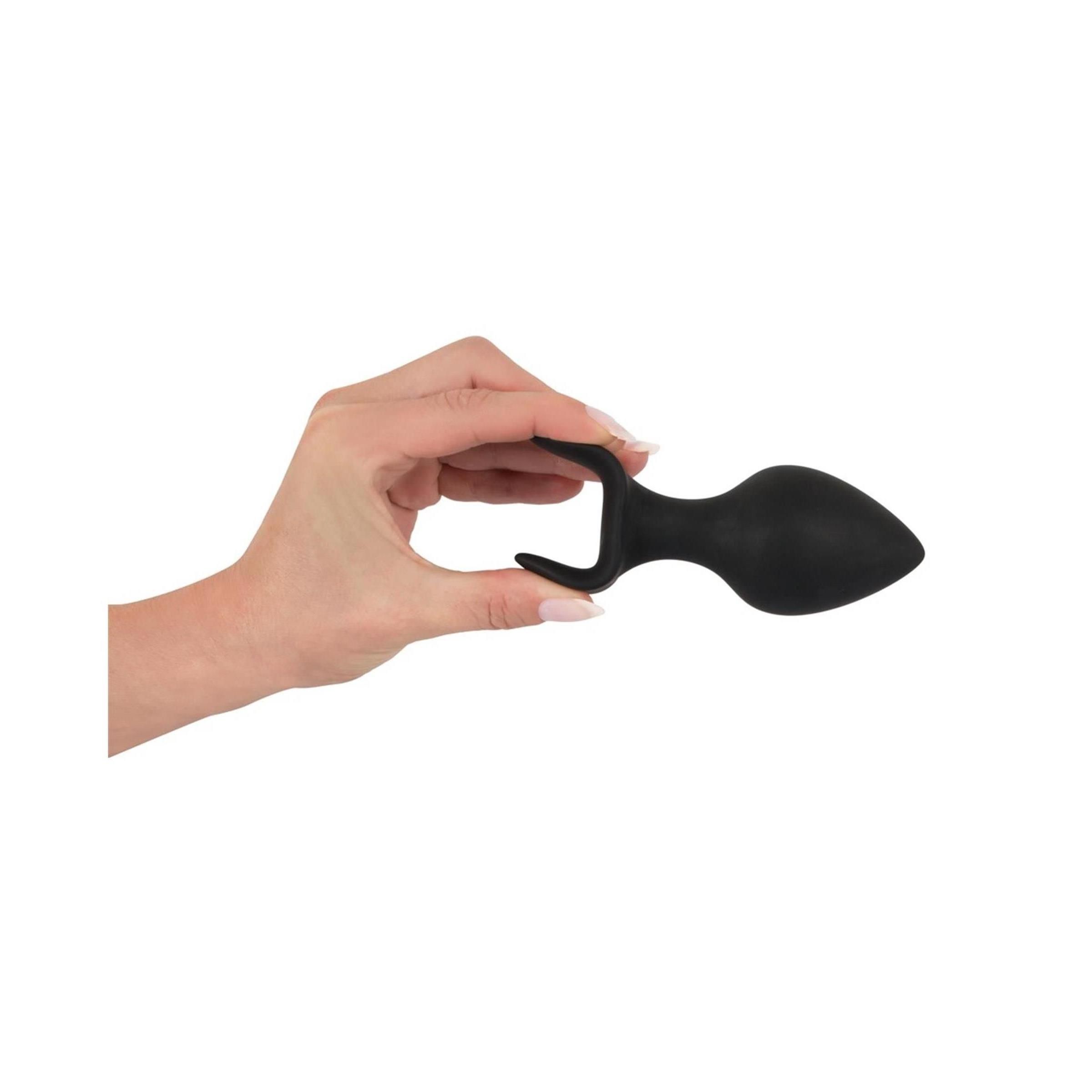 Hand hält einen schwarzen Anal-Trainer. Konische Spitze, gebogene Basis.