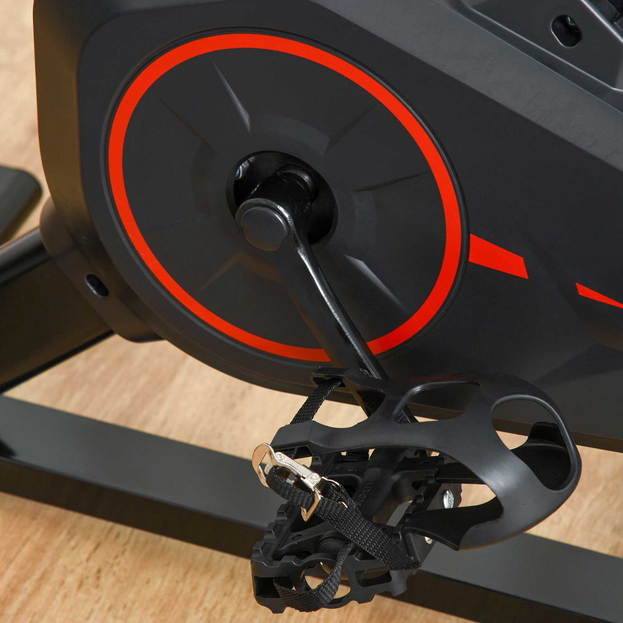 Nahaufnahme der Pedale eines Fitness-Fahrrads. Schwarze Farbe mit Riemen. Auf Holzboden.