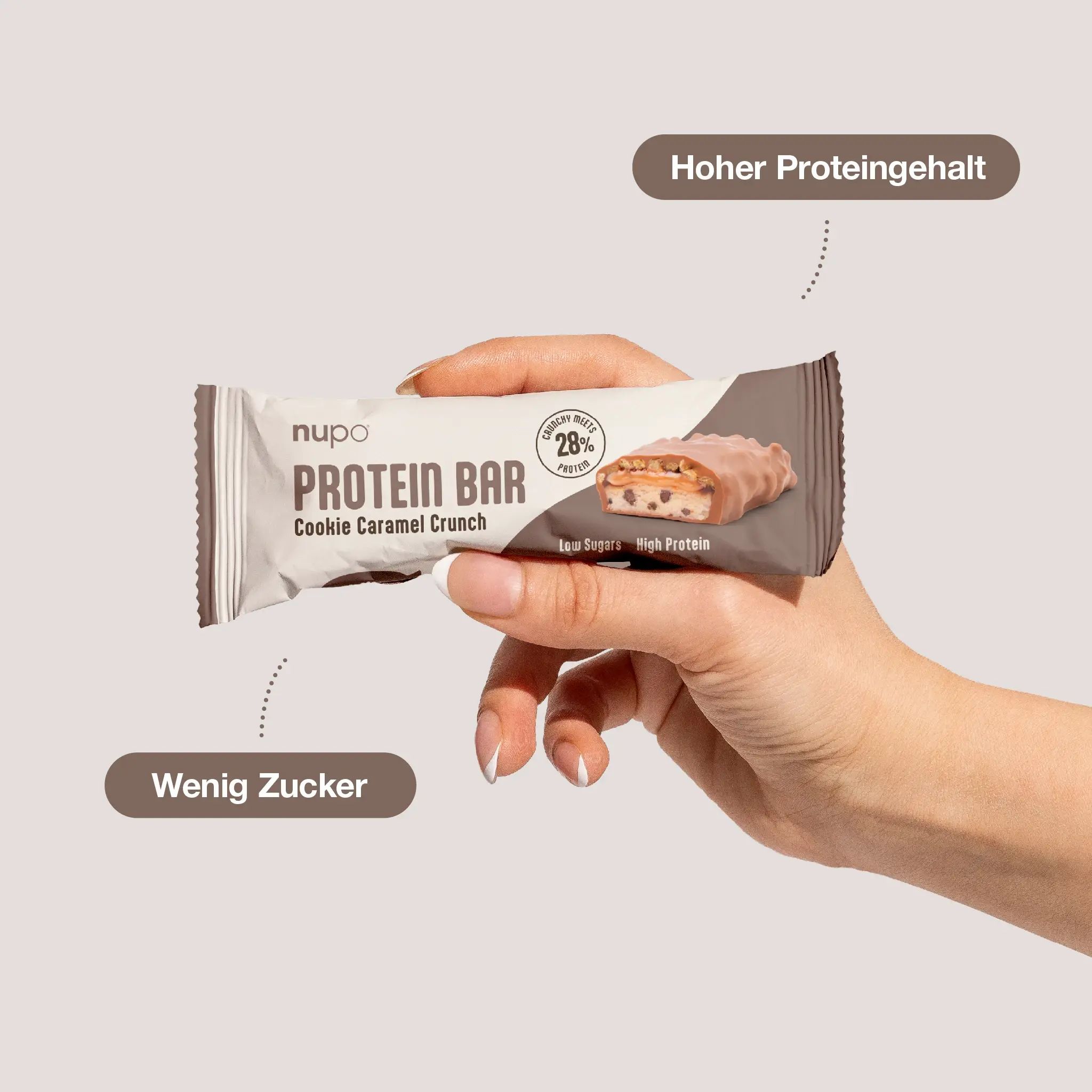 Hand hält Proteinriegel Cookie Caramel Crunch. Produktbezeichnung und Marke sichtbar. Text: Wenig Zucker, Hoher Proteingehalt.