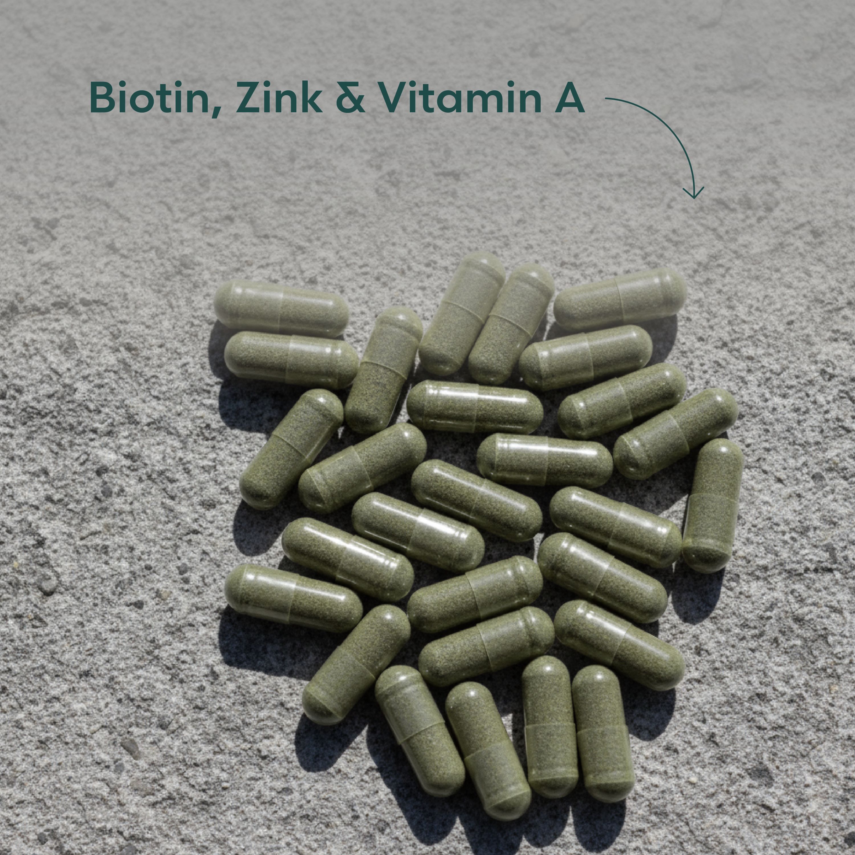 Haufen von grünen Kapseln auf grauem Untergrund. Pfeil mit Aufschrift: Biotin, Zink & Vitamin A.