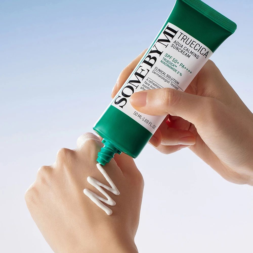 Hand drückt Sonnencreme aus einer Tube. Text: SOMEBYMI, TRUECICA Aqua Calming Suncream, SPF 50+ PA++++. Creme auf der Haut.