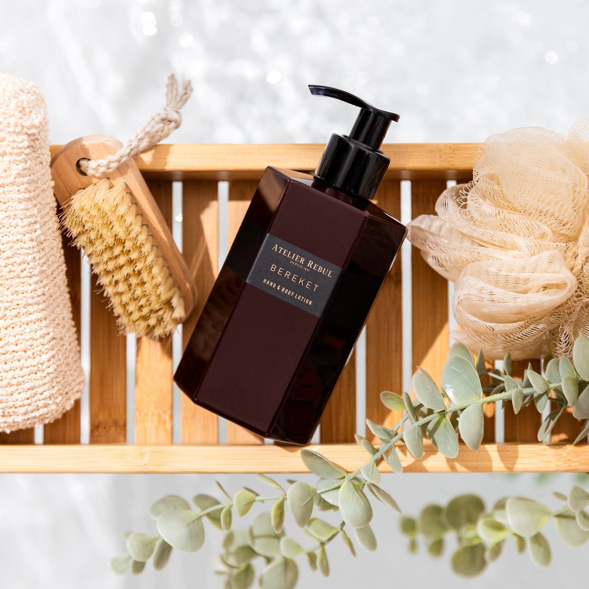 Bordeauxfarbene Lotionflasche mit schwarzem Pumpkopf. Aufschrift: Atelier Rebul Bereket Hand & Body Lotion. Auf Holzablage.