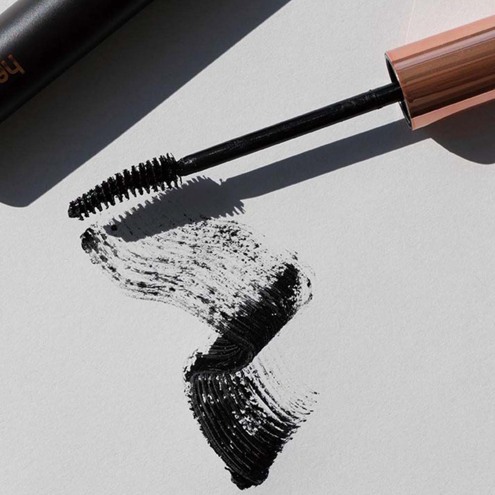 Mascara-Applikator mit Bürste und schwarzer Mascara-Spur auf weißem Papier. Der Applikator hat eine kupferfarbene Kappe.