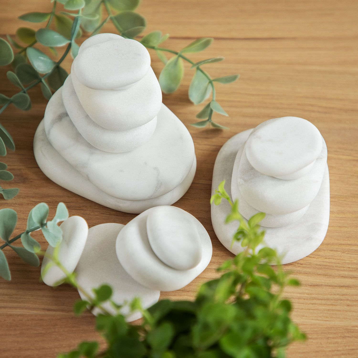 Mehrere weiße, ovale Steine auf Holzuntergrund, arrangiert. Grüne Pflanzen im Hintergrund.