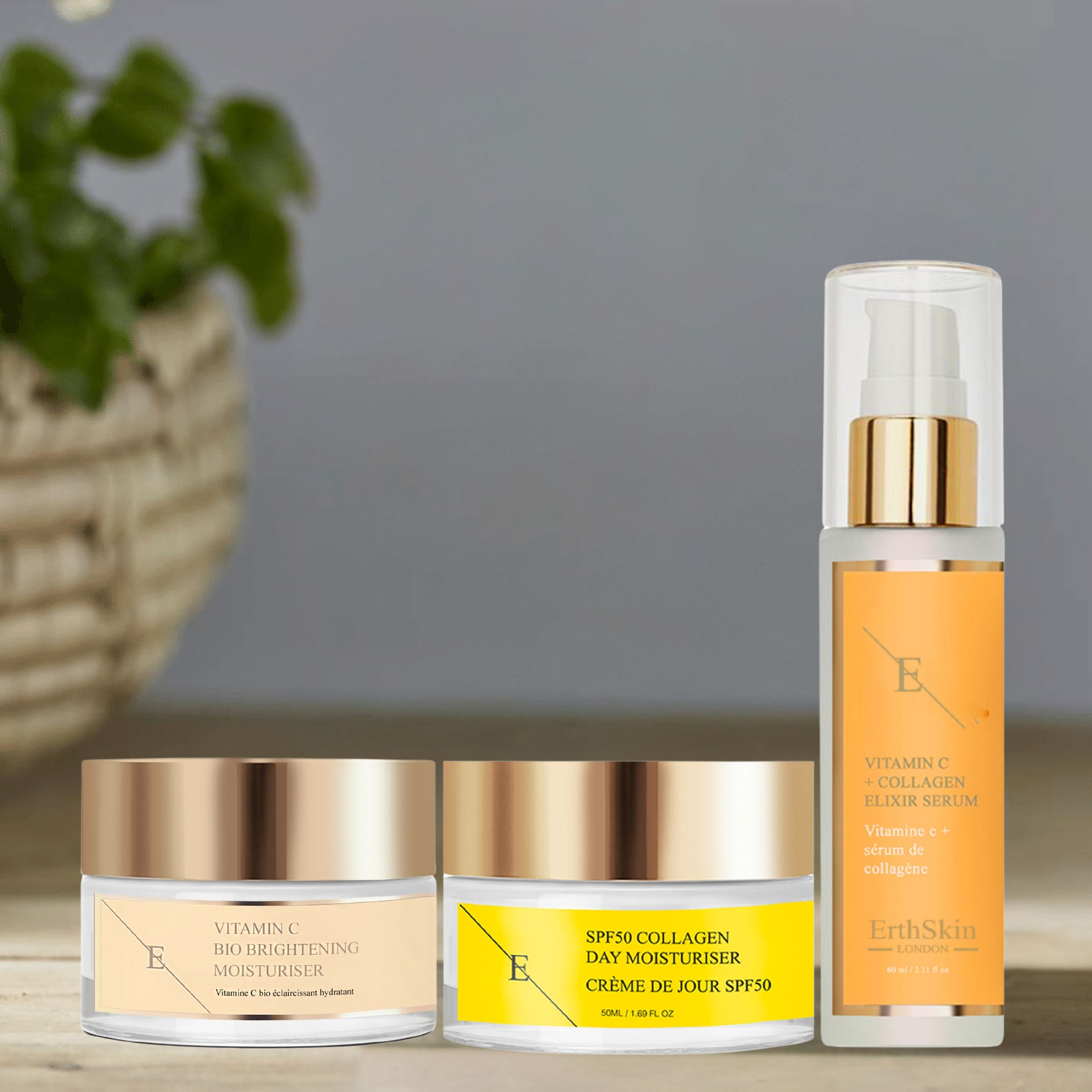 Drei Hautpflegeprodukte: Serum, Tagescreme und Feuchtigkeitspflege. Goldfarbene Deckel, gelbe Etiketten. Hintergrund: Pflanze.