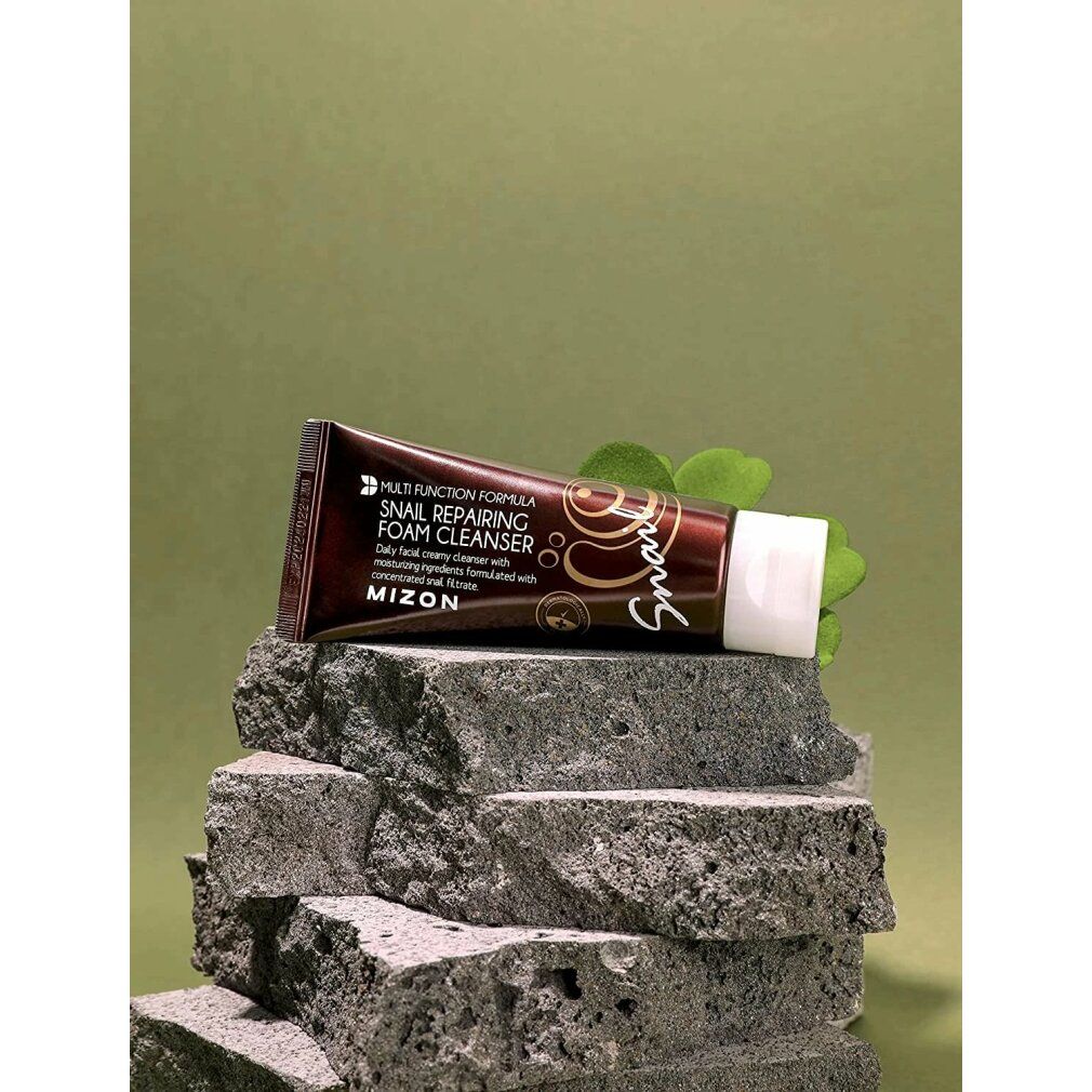 Braune Tube mit weißem Verschluss auf Steinen. Aufschrift: MIZON Snail Repairing Foam Cleanser. Text und Schnecken-Illustration.