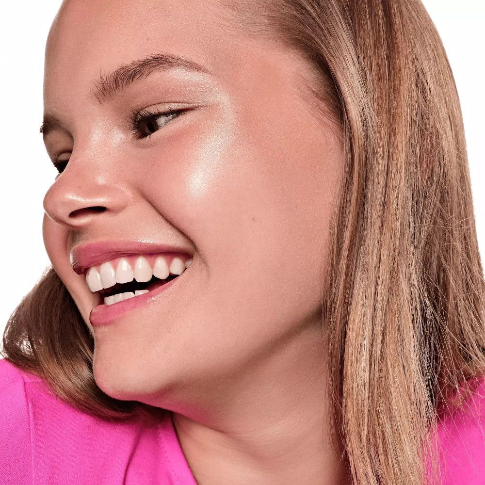 Gesicht einer lächelnden Person mit Highlighter. Haut glänzt. Rosa Lippen.