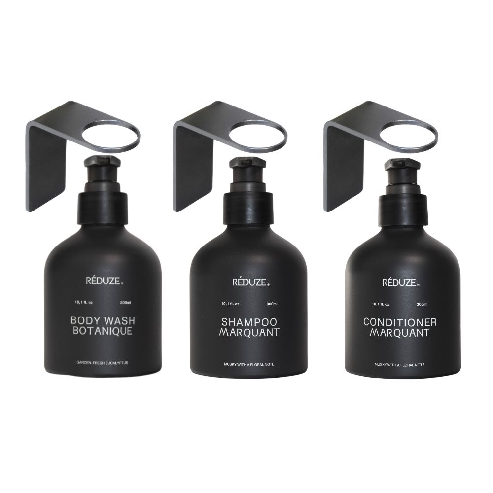 Drei schwarze Flaschen mit Pumpaufsatz und Wandhalterung. Beschriftung: Body Wash, Shampoo, Conditioner. Marke: RÉDUZE.
