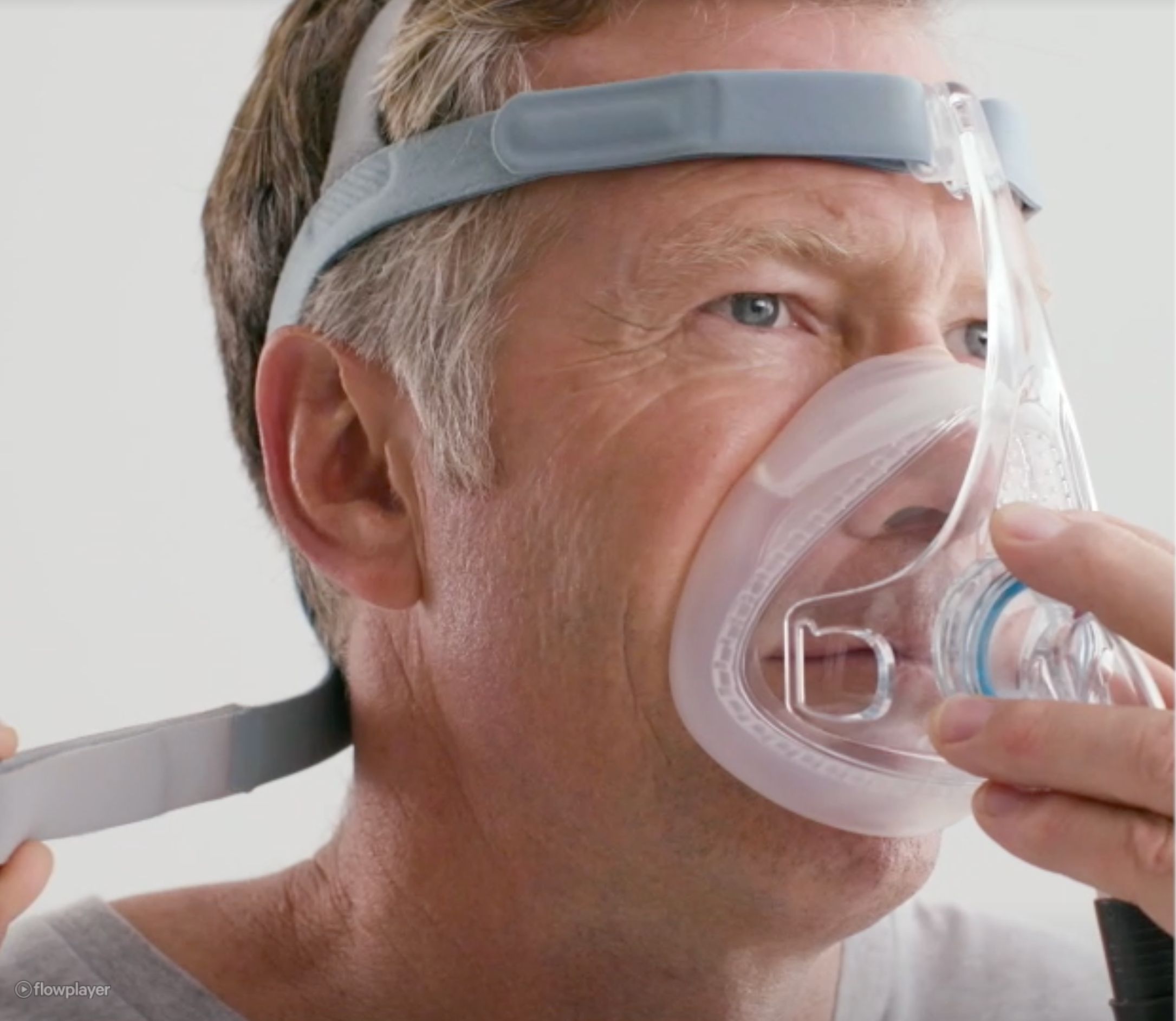 Nahaufnahme eines Mannes mit CPAP-Maske. Maske bedeckt Nase und Mund. Kopfband und Anschlüsse sichtbar.