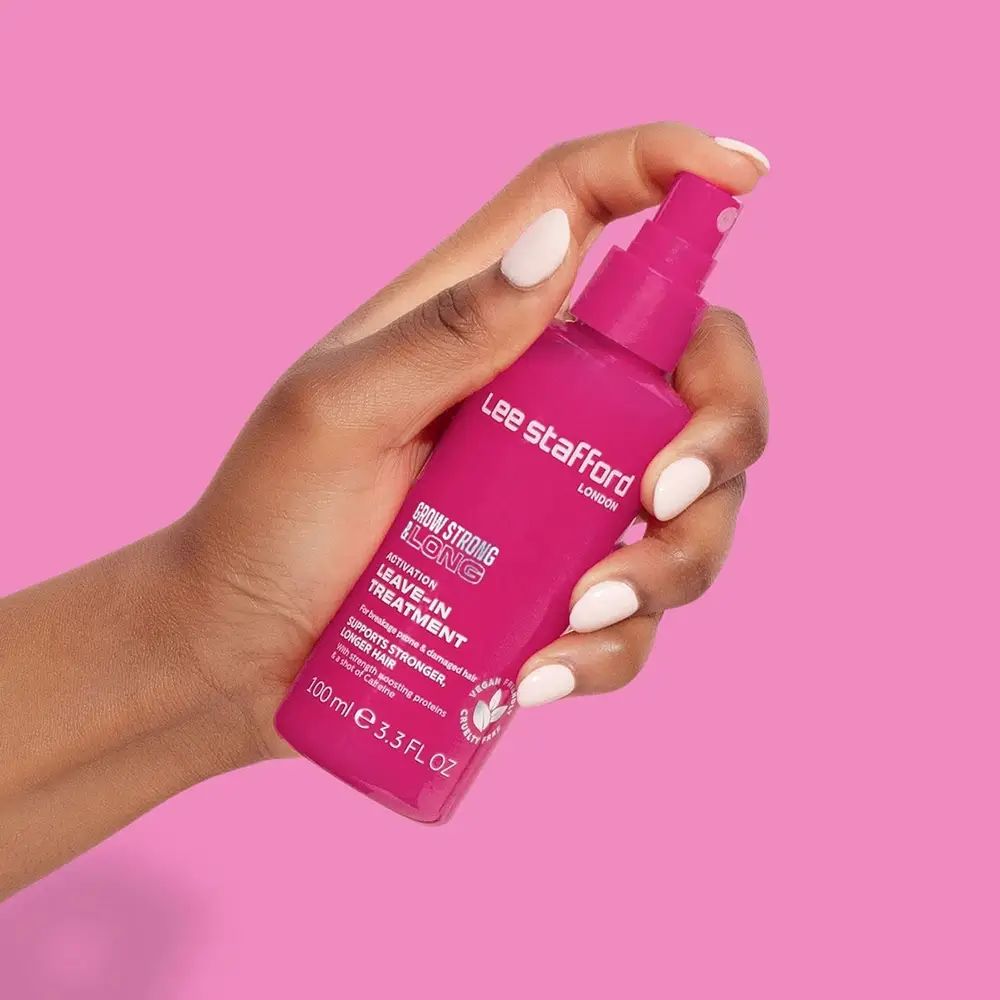 Rosa Sprühflasche, gehalten von einer Hand mit weißen Nägeln. Aufschrift: Grow Strong & Long Leave-In Treatment. Marke: Lee Stafford.