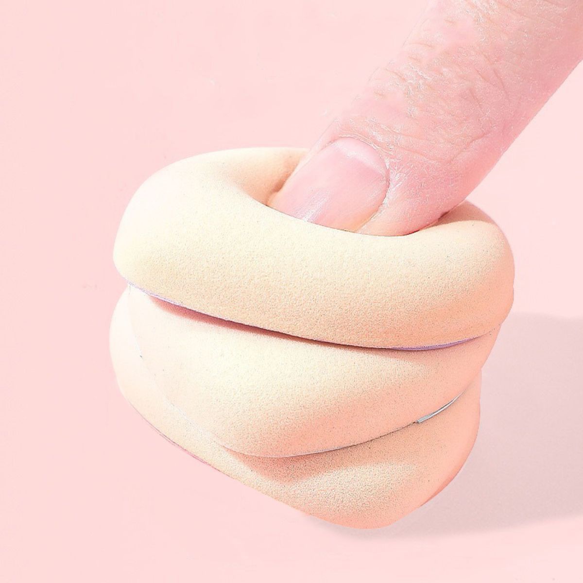 Ein hellbeiger Make-up-Schwamm wird von einem Finger zusammengedrückt. Der Schwamm ist weich und flexibel.