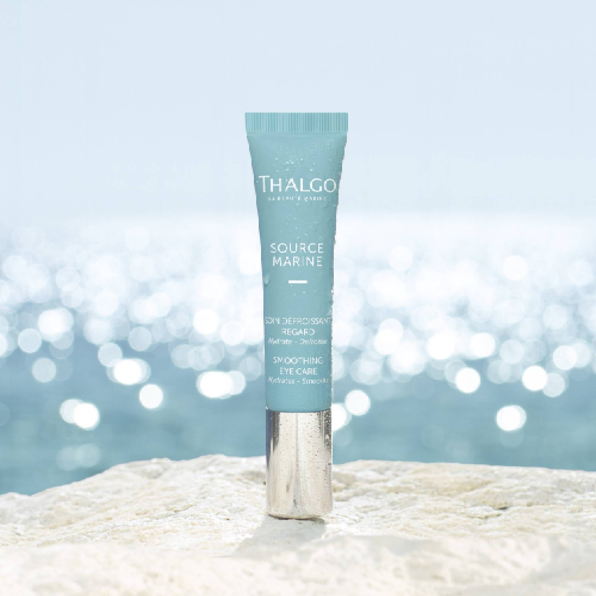 Türkisfarbene Tube mit silbernem Verschluss, vor verschwommenem Meer. Aufschrift: THALGO, SOURCE MARINE, SOIN DÉFROISSANT REGARD, Smoothing Eye Care.