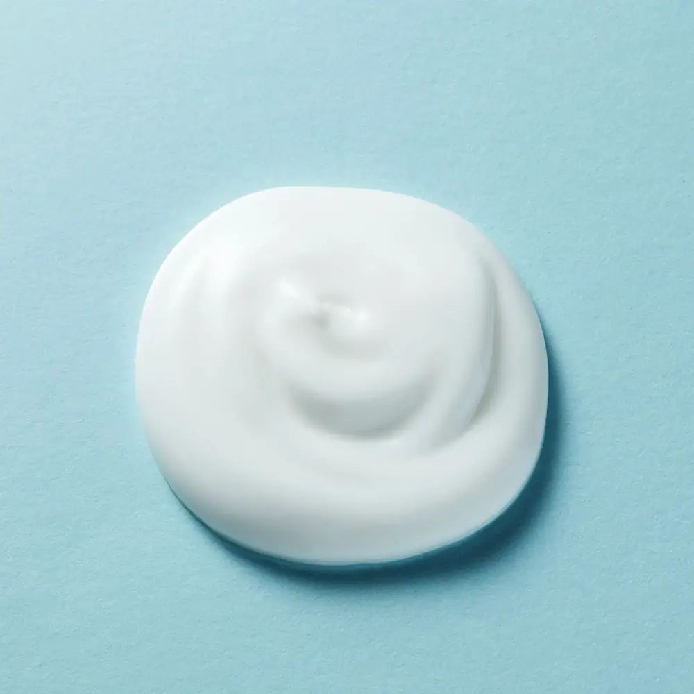 Nahaufnahme eines weißen, cremigen Produkts auf blauem Hintergrund. Die Creme ist spiralförmig aufgetragen.