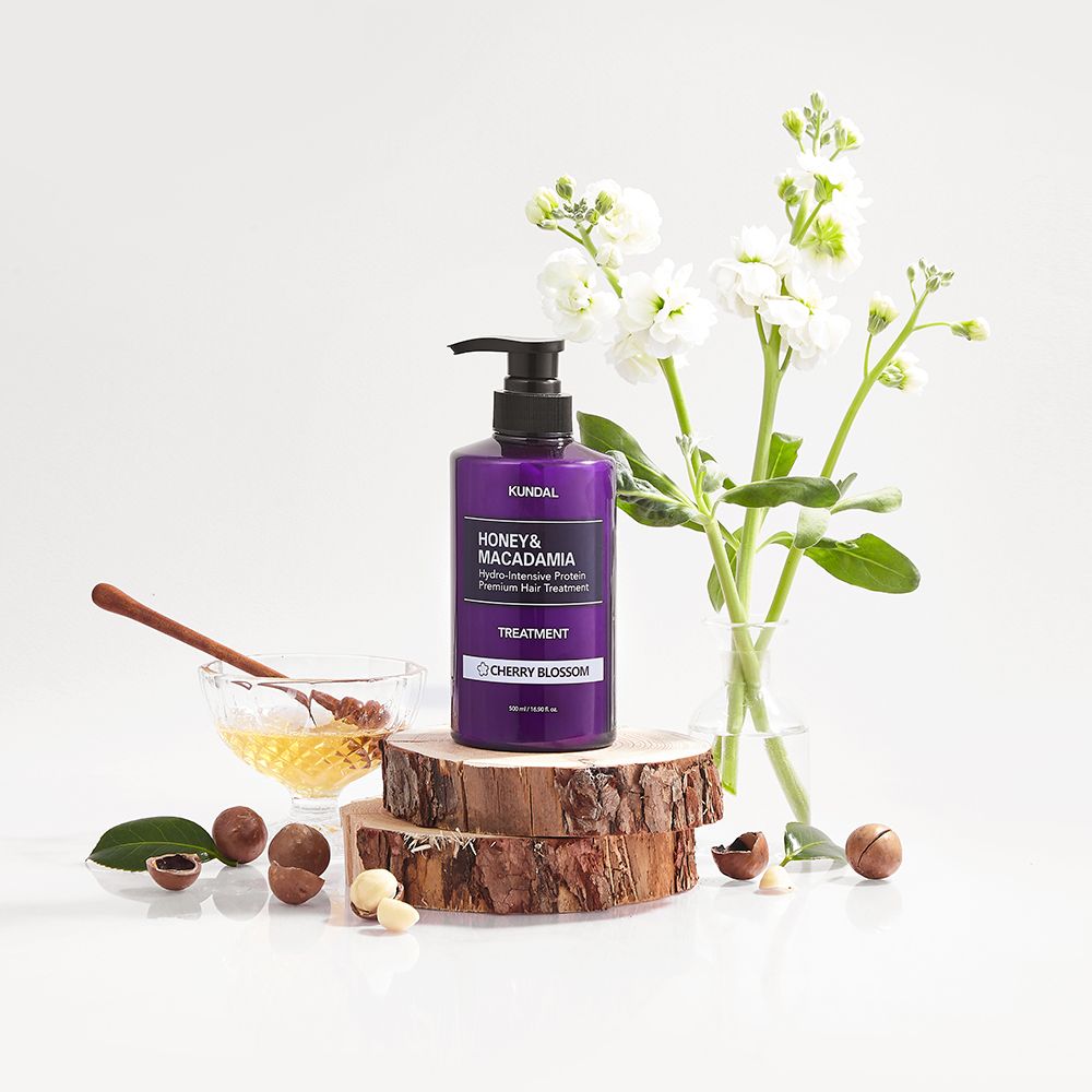 Violette Flasche mit Pumpe, KUNDAL Protein-Haarkur, Honig & Macadamia Cherry Blossom. Auf Holzscheiben, mit Blüten und Honig.